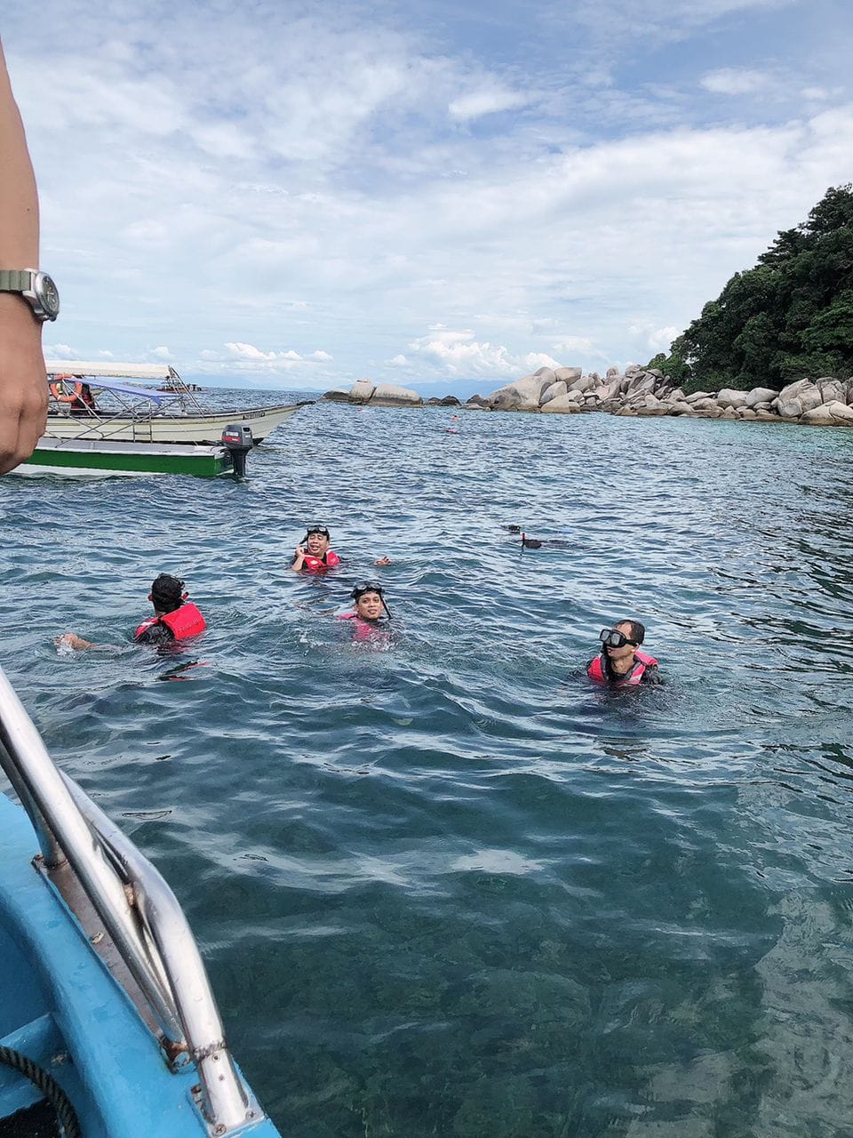 Guests snorkelling together beside the boat near the rocky shoreline